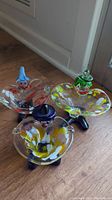Photo of three colorful hand blown clown ashtrays on wood floor, showing different clown hat colors and bases
