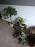 Artificial tree alongside two artificial plants and wooden bench against a wall on carpeted floor