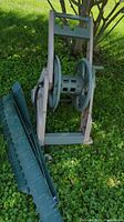 Side angle of beige-green plastic garden hose reel with winding crank and black hose alongside green plastic lawn edging showing cracking.