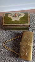 Florentine dome box with curved lid, floral bouquet painted on green surface, detailed gold gilt border, alongside rectangular gold gilt purse with embossed designs and rope handles.