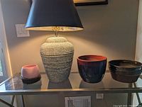 Photo of lamp and three planters on a glass table, showing the speckled lamp base with black shade and the different colors and finishes of the planters.