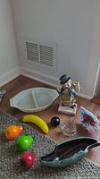 Photo showing the full lot including five hand blown glass fruit (lime, pepper, banana, plum, strawberry), Pyrex divided bowl, mid-century ashtray, art glass whale, art glass trumpet, and red skeleton clown figurine.