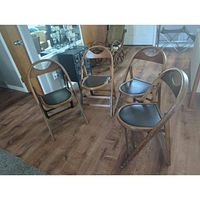 Four mid-century wooden folding chairs arranged in a semicircle, showing black vinyl/leather seats and rounded wooden frame backs with built-in handles.