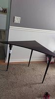 Side view of a black triangular mid century modern corner table with three tapered legs on carpeted floor