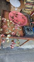 Two metal flower wall decorations with pink and brass petals, a pink tin platter with botanical design, and a timer on a wooden table.