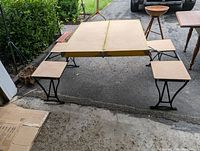 Portable wooden tabletop with four attached folding chairs set up outdoors on pavement.
