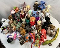 Group shot of 50 assorted TY Beanie Babies arranged around a green apple for size reference