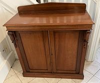 Front view of the antique wooden cupboard showing solid construction and two paneled doors with carved Regency style details on the vertical sides.
