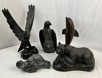 Five animal sculptures displayed together: stone bear, wooden seal, wooden eagle with spread wings, stone hawk, and wooden dolphin.