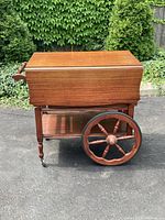 Front view of wooden butlers tea cart with leaves down showing glass bottom tray and large wooden wheels with caster wheels.
