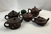 Five Zisha clay teapots displayed with green apple for scale
