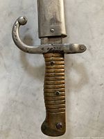 Close-up of brass ribbed grip, curved quillon and ricasso with inspection and serial markings