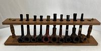 Wooden pipe rack with ten inserted pipes against white background