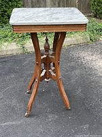 Full view of the marble topped wooden table showing the Eastlake style wooden base with four curved legs and caster wheels.