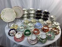 Overall view of 32 assorted teacups and saucers displayed with two decorative plates on stands