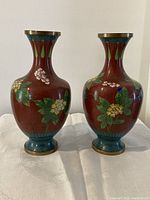 Front view showing pair of matching cloisonne vases with floral enameling on a red background and gilt brass accents.