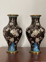 Front view of the matching pair of cloisonne vases showing floral cherry blossom and bird design on a black background with blue rock detail at base.