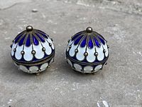 Pair of round trinket boxes made of gilt silver with blue and white enamel decoration, placed on a stone surface.