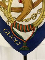 Close-up of corner showing gold 'Gucci' logo on navy border with equestrian bit and tassel motif