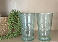 Pair of clear green recycled glasses embossed with an oval cow and AMICI logo shown side by side