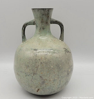Photo showing round metal vase with two handles and patina surface against white background