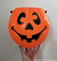 Front view of the bright orange plastic Jack-O-Lantern candy bucket showing smiling carved pumpkin face with black paint details.