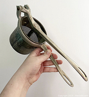 Close-up of the vintage metal press with perforated basket and long handles showing condition and design