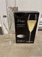 Set of four tall, clear champagne glasses displayed with their original black box. The box highlights the brand Luigi Bormioli, model Prestige and capacity of each glass (9 oz/27 cl).