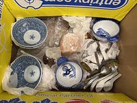 Top-down view of mixed bowl types, ceramic spoons, metal utensils, and wrapped Himalayan salt lamp in a box