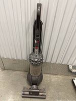 Front view of Dyson DC77 upright vacuum cleaner showing full body, dust container, handle, and cleaning head.