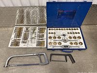 Overall view of tool and die set including taps, dies, and two hacksaws.