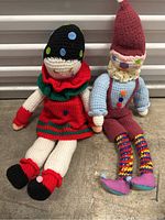Two vintage crochet dolls, one in red dress and one dressed as gnome, placed on concrete floor.