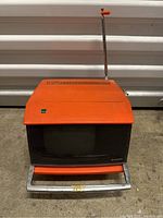Front view of orange Sharp portable TV with black screen, metal handle, and antenna extended.
