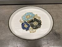 Front of oval serving plate showing blue, light blue, and black floral design with gold accents