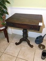 Front view of the antique pedestal table showing the rectangular top, drawer with knobs, and the base.