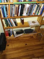 Full view of lower three shelves on a wooden bookshelf filled with various hardcover and paperback books.