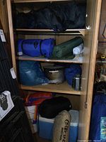 Cabinet interior showing folded sleeping bags, cooler, large pot, kettle, rolled camping bags and folded items