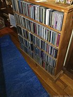 Wooden shelf filled with multiple rows of CDs in jewel cases.