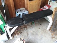 Side view of Northern Lights exercise bench with white metal frame and black padded seat and backrest, located in a garage setting.