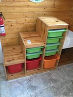 Three quarter front angle of the wooden step-style shelving with colored bins showing natural wood finish and arrangement of bins