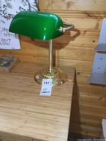 Front and side view of the green glass and brass bankers lamp on a wooden surface.
