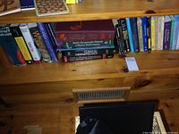 Books on a wooden shelf showing various medical and self-help book titles including clinical dermatology, human malformation patterns, and examination manuals.