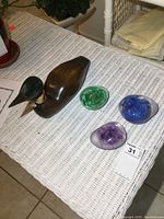 Full set showing wooden duck decoy and three colored glass paperweights arranged on a wicker surface.