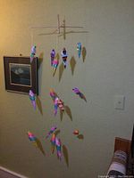 Full view of the parrot mobile hanging in a corner of a room, showing 12 colorful wooden parrots suspended from threads on a wooden structure.