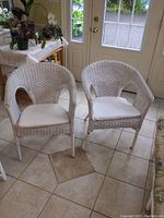 Pair of white wicker tub chairs with white cushions, viewed from front showing overall condition and shape.