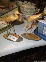Pair of wooden bird carvings on a table with porcelain tureen in background
