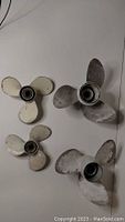 Overview photo showing all 4 boat propellers, two painted white and two unpainted metal with wear and oxidation.