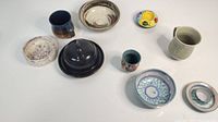View of all 9 pottery pieces on a white surface including bowls, cups, plates, and covered container.