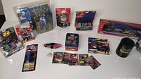 Wide shot showing the full assortment of NASCAR collectibles including diecast cars, figurines, trading cards, and branded merchandise arranged on a white background.