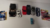 Overview of eight toy cars in various colors and conditions including two packaged items on far right and several loose cars.